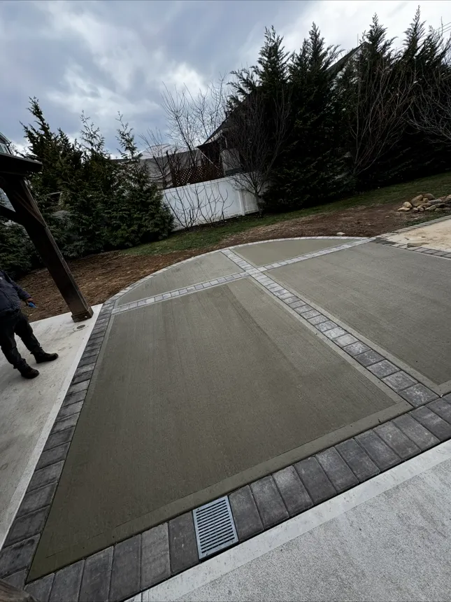 Curved concrete patio with paver border and drainage grate installed in Suffolk County NY
