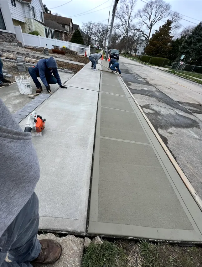 Crew finishing a new concrete sidewalk and driveway apron on a Long Island residential street